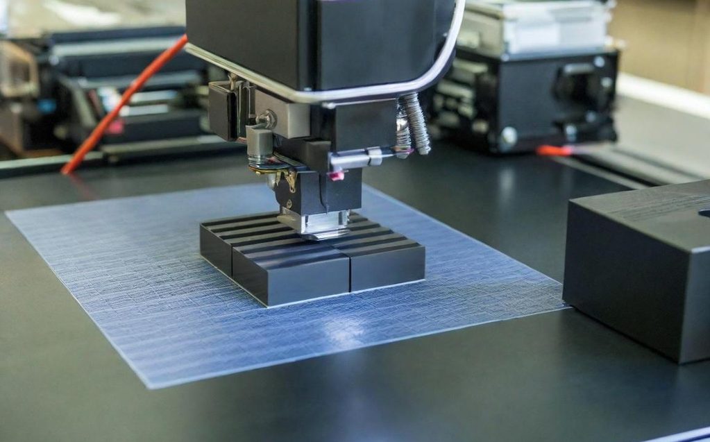3D printer creating a black object on a blue surface.